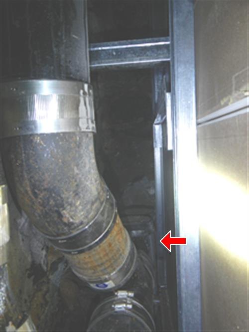 Large cast iron drain elbow with banded couplings turning down beside a framed wall cavity, red arrow pointing into the enclosed space