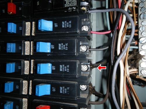 Rows of circuit breakers inside an open electrical panel with a red arrow at a breaker terminal wired with an aluminum conductor