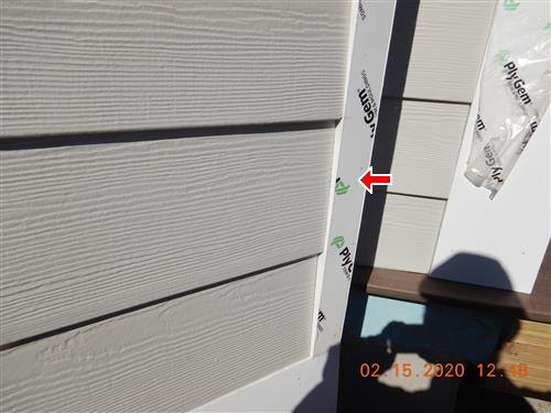 Fiber cement siding at an outside corner with a red arrow at vinyl trim still covered in branded protective film