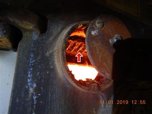 Glowing orange fire box interior seen through an opening in a rusted boiler jacket, red arrow, date stamp