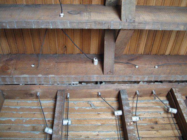 Knob and tube wiring beneath floor joists: white ceramic knobs fixed to the timber with single conductors threaded through and around them.
