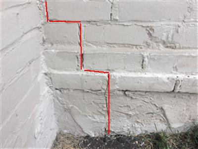 A step crack in painted masonry, traced in red on the report photograph.