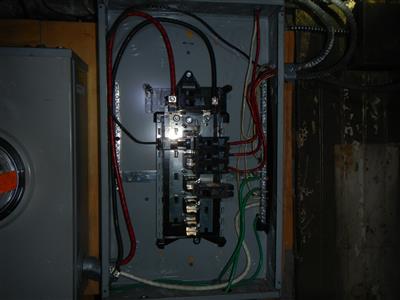 An electrical distribution panel with the cover removed, breakers and conductors visible.