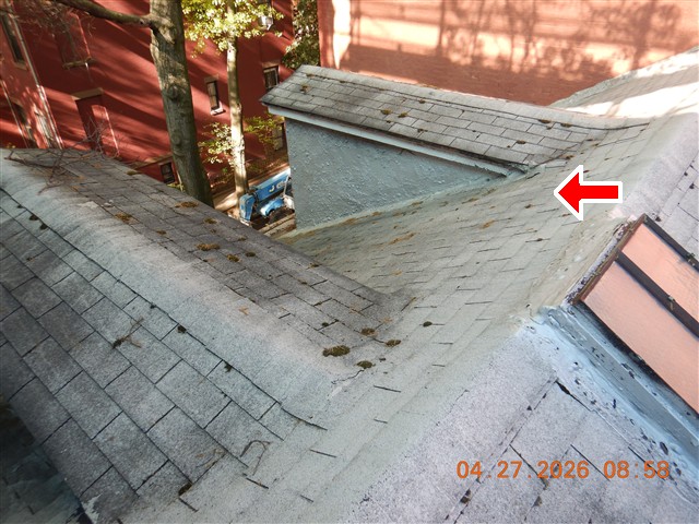A roof slope meeting a parapet, with the flashing detail marked by an arrow.