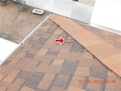 Brown shingle roof seen from above with a red arrow at a raised shingle near the capping; patio below.
