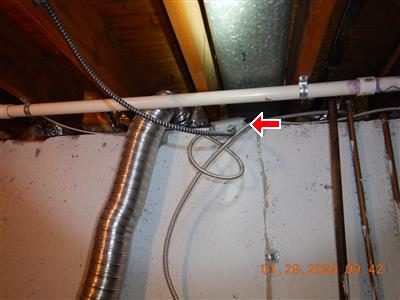 Basement ceiling with a white pipe, flexible duct and a loop of armoured cable at a junction box, marked by a red arrow.