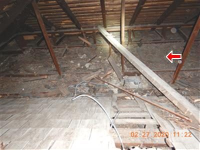 Attic with loose boards and construction debris strewn across the joists, red arrow pointing at a leaning plank.