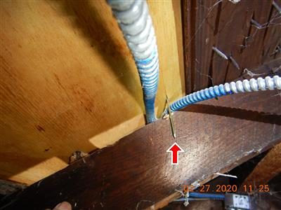Blue-armoured BX cable beside a wooden rafter with a nail point protruding through the wood, red arrow.