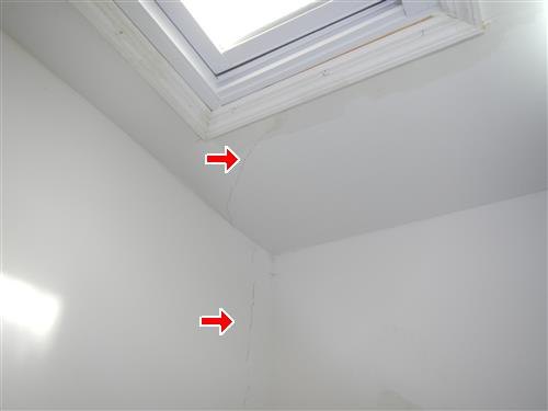 A skylight well in a sloped top-floor ceiling with hairline cracks marked by red arrows.