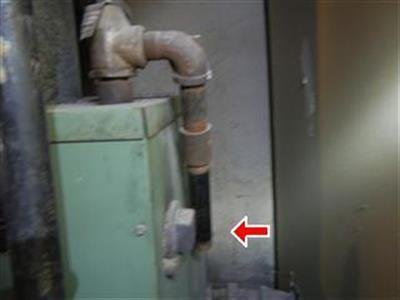 Older green boiler with corroded piping and red arrow at a flexible connector
