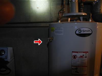White tank water heater in a basement with red arrow at a side valve fitting