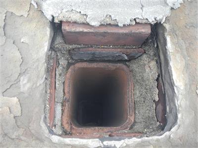 View down into a clay-lined chimney flue with cracked concrete and debris at the top