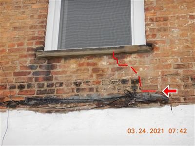 Brick wall below a window sill with a stair-step crack traced in red dashes, marked with a red arrow.