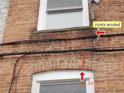 Brick wall between two windows with a crack traced in red under the upper sill and a label reading joints eroded.