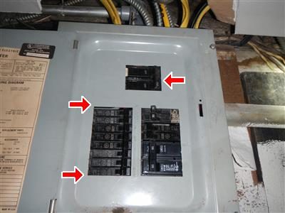Grey breaker panel with its cover on, three red arrows pointing at breakers partly hidden by the cover.