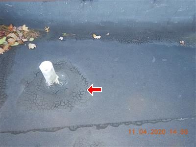 Flat roof surface with a small white pipe penetration and cracked, crazed tar around its base, red arrow.