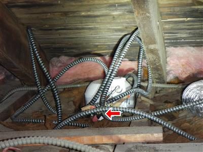 Recessed light housing in an attic with armoured cables around it, red arrow pointing at exposed conductors.