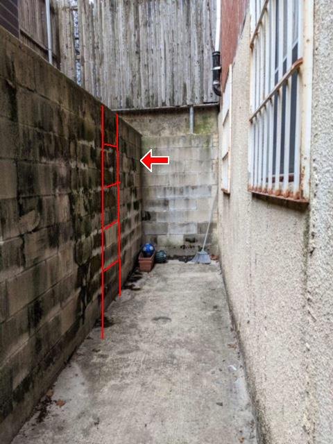 A narrow side passage between two buildings with step cracks traced in red on the block wall.