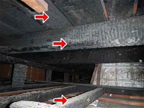 Charred wood floor joists and beam viewed from below, three red arrows at burned areas