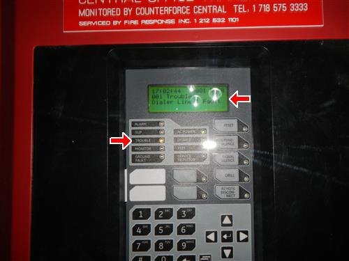 Fire alarm control panel keypad with red arrows at trouble light and display message