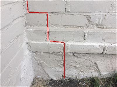 A painted brick foundation corner with a step crack traced in red.