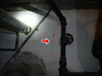 Basement wall with dashed red line and arrow tracing a vertical crack near piping