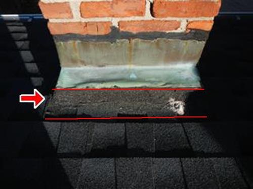 A brick chimney meeting an asphalt roof, the flashing seam marked with red lines.