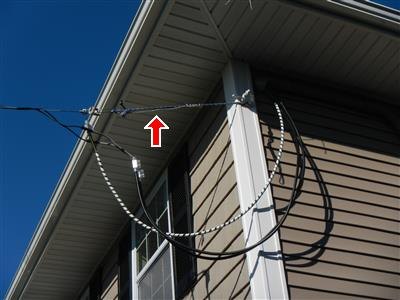 Overhead service wires attached at the corner eave of a house, red arrow pointing up