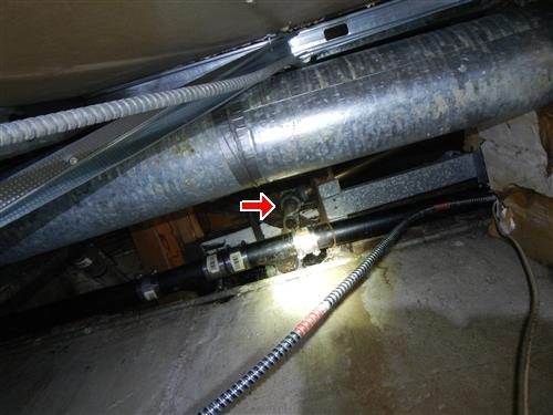 Plumbing under a floor in a basement ceiling with a red arrow at a tub trap beside a flexible duct.