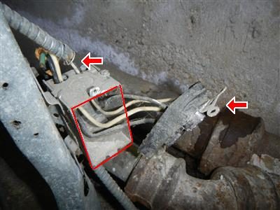 Loose outlet box with wires exposed next to corroded pipes, marked with a red box and two red arrows.