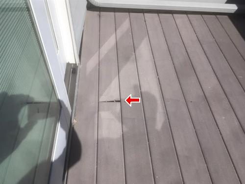 Grey composite deck boards beside a sliding door with a red arrow at a cracked, raised board.