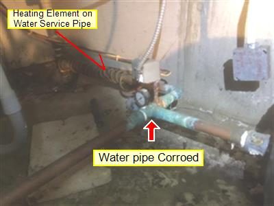 Green-corroded copper water service pipe near the base of water tanks, with red labels and an arrow.