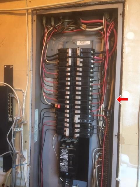 Open main electrical panel with two columns of breakers and neatly routed red, black and white wires, marked with a red arrow.