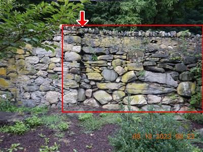 Dry stone retaining wall with moss, a red rectangle around the eroded section and a red arrow at the top.