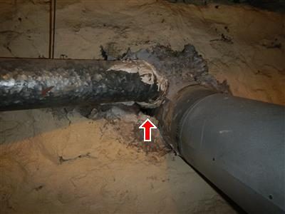 Two flue pipes entering a basement wall with a red arrow pointing to an open hole in the cement around them.