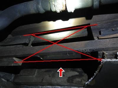 Dark basement ceiling with a red X marked across a gap between floor joists and a red arrow pointing up at it.