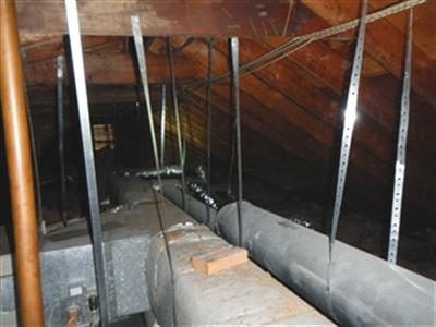 Attic interior with insulated ductwork running along the floor between rafters and metal hanger straps.
