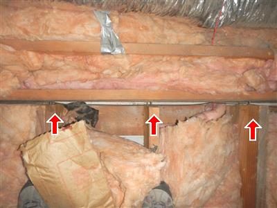Attic framing with pink insulation and red arrows pointing to the end joist where nails have pulled loose.