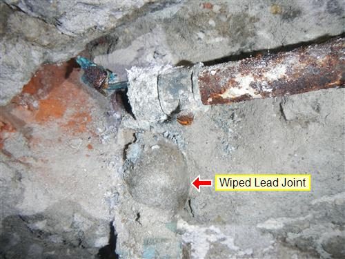 Old corroded water pipe entering a rough stone foundation wall with a bulbous joint labelled Wiped Lead Joint.