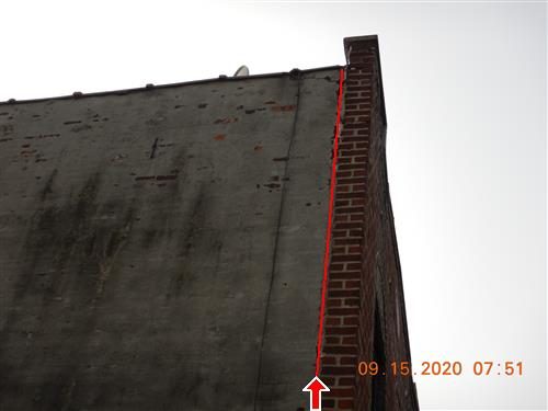 Looking up a tall brick side wall meeting the front brick wall, with a red line tracing a crack down the corner.