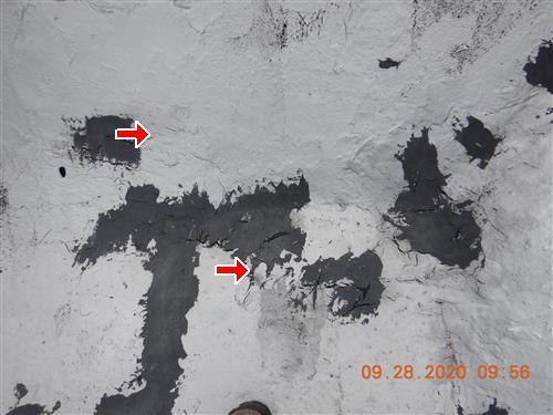 A silver-coated flat roof surface with multiple dark patched areas marked by red arrows.