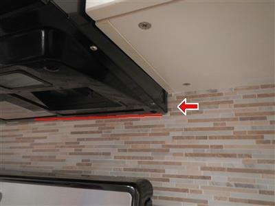 Underside of a black range hood above a tiled backsplash, with a red line and arrow markup.