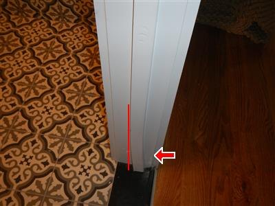 White door casing with a red vertical line and arrow at its base, between tile and wood floors.