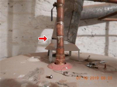 Copper pipe rising from a water heater top, red arrow at a soldered joint, orange date stamp.