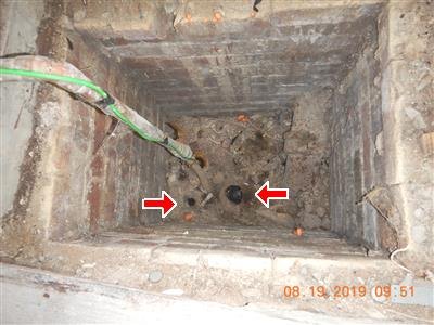 Brick-lined pit below a floor with drain piping and two red arrows, orange date stamp.