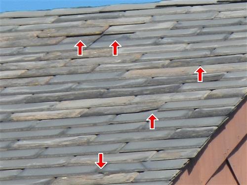 A slate-type shingle roof with several slipped or broken pieces marked by red arrows.