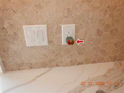 A kitchen backsplash with an outlet tester plugged into a receptacle, arrowed.