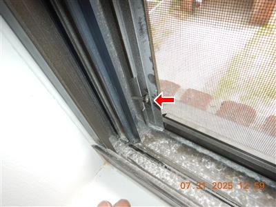 Corner of a metal window frame with insect screen, red arrow at the frame joint, date stamp.