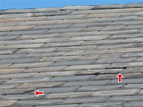 Sloped roof of thick gray shingles with two red arrows at displaced pieces.