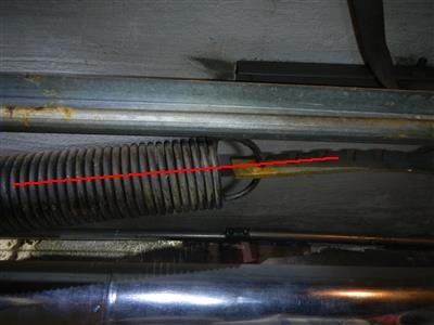 Garage door torsion spring and track seen from below, with a red line drawn along the spring.
